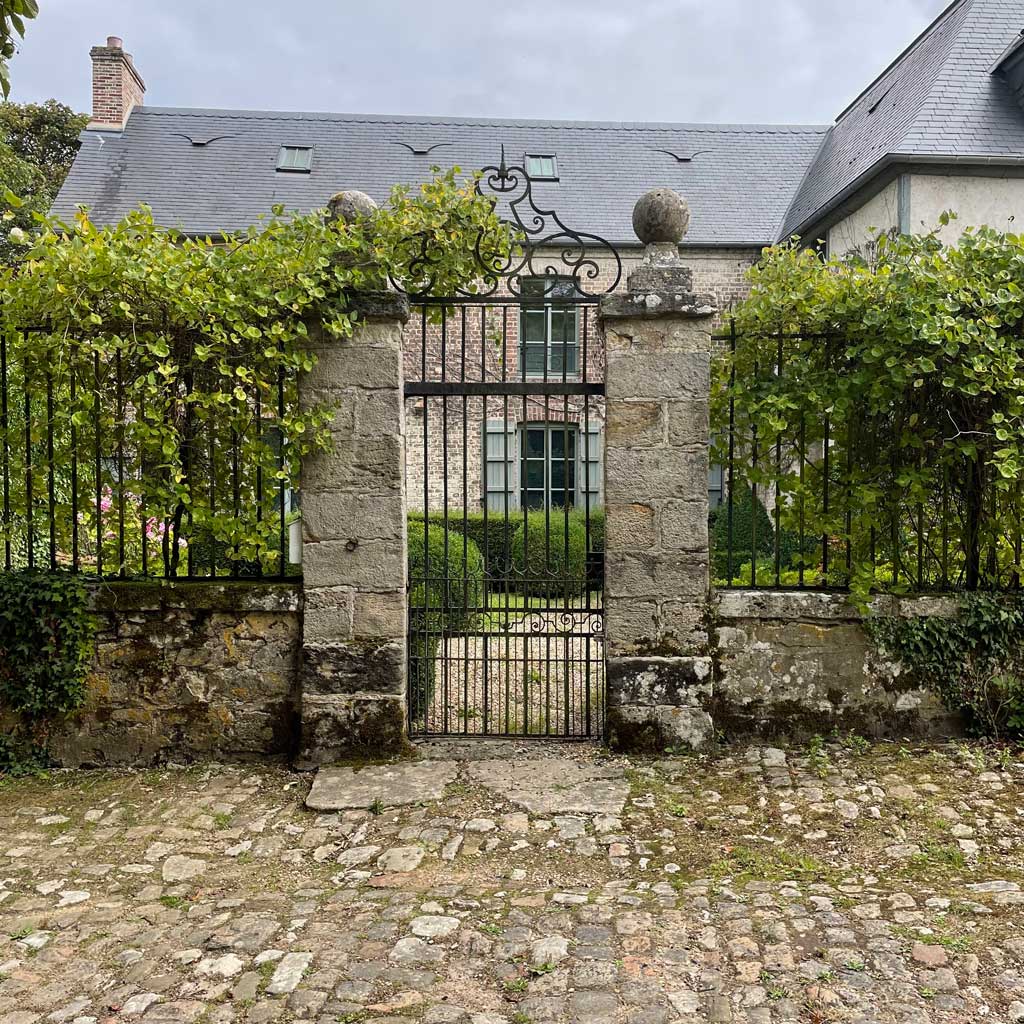 Garden design in Normandy. Entrance gates and paving with stonework and ironwork in French garden design style.