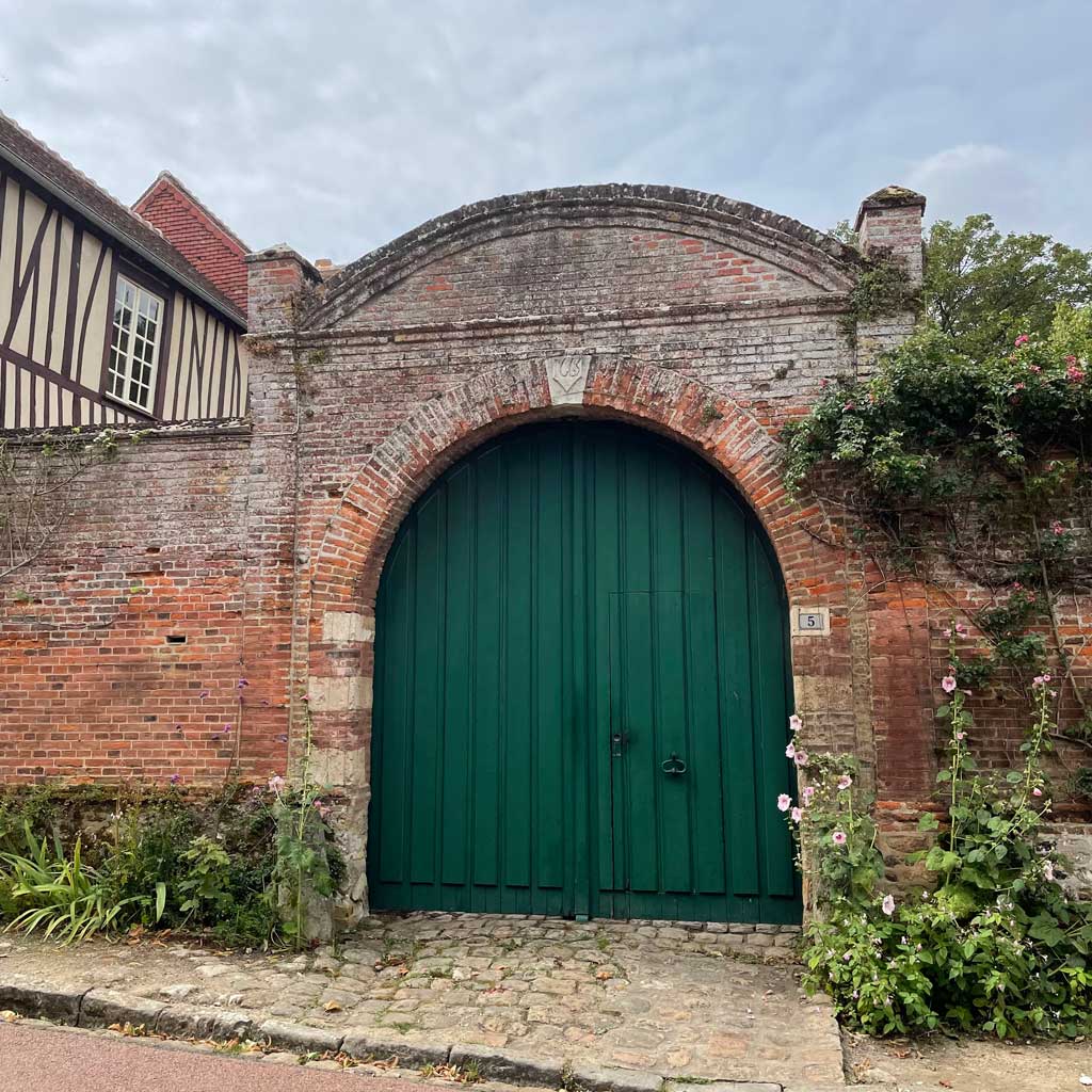 An old grand red brick wall and arch surrounding large green wooden gates
